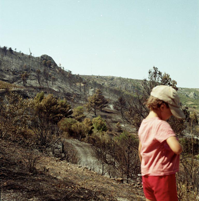 Enfant de dos, avec une casquette, au premier plan d'un paysage de montagnes brûlées