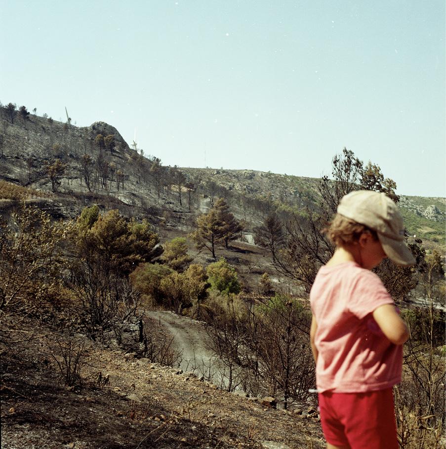 Enfant de dos, avec une casquette, au premier plan d'un paysage de montagnes brûlées