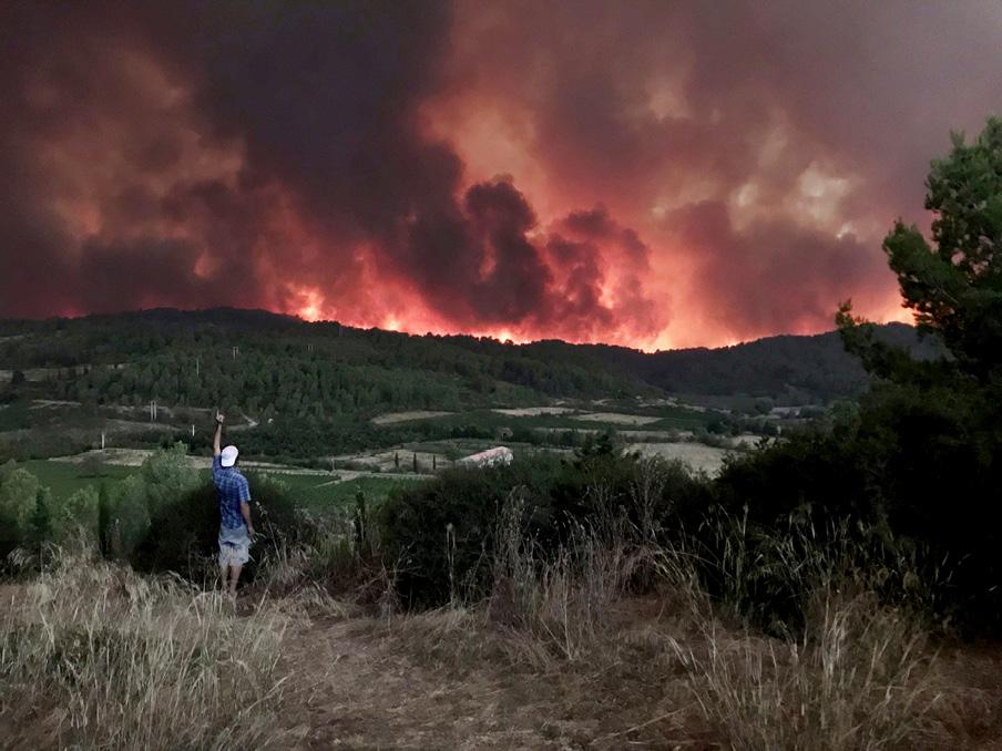 paysage de montagne avec un grand incendie au fond et une personne dos au premier plan avec une casquette blanche à l'envers et la main gauche levée