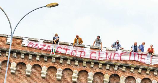 Six personnes au-dessus d'une grande banderole en haut d'un monument de briques. La banderole dit "Gaza stop génocide"