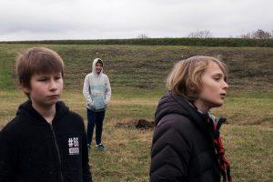 trois enfants dans un espace de pelouse et gravier, regardant à droite hors champ