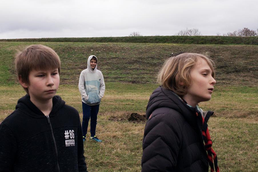 trois enfants dans un espace de pelouse et gravier, regardant à droite hors champ