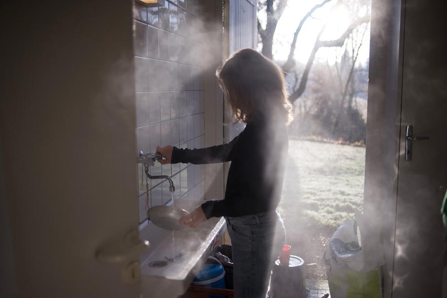 enfant se servant d'un robinet dans un bâtiment avec vue en fond sur des arbres et de l'herbe
