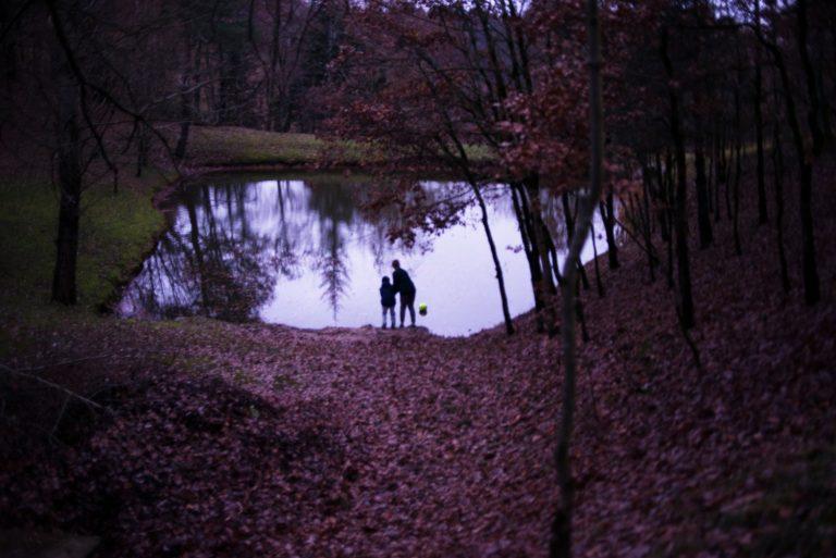 photo d'un étang dans une forêt, avec deux silhouettes d'enfants de dos, proches de la rive