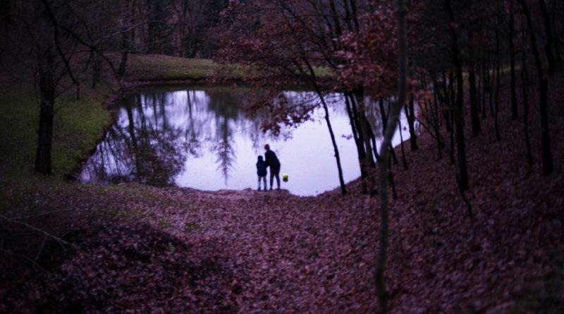 photo d'un étang dans une forêt, avec deux silhouettes d'enfants de dos, proches de la rive