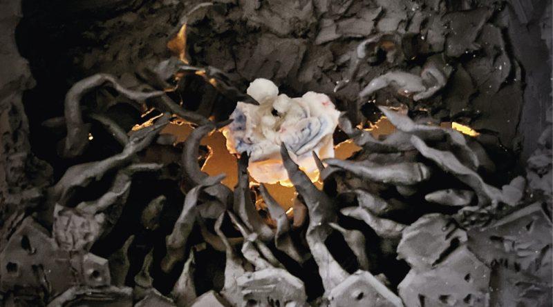 photo d'une sculpture : personnages en blanc au milieu d'un village noir. Flammes.