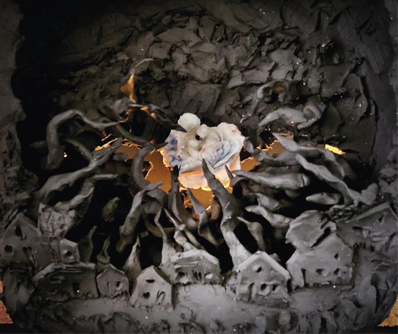 photo d'une sculpture : personnages en blanc au milieu d'un village noir. Flammes.