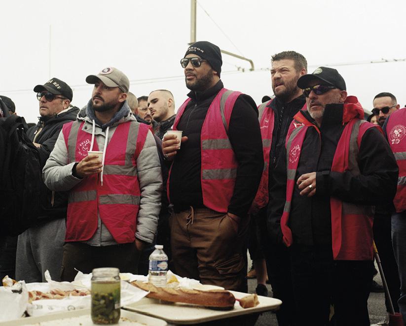 Cinq hommes avec des chasubles de syndicats, regardant vers la gauche. Au premier plan, une table avec baguette, jambon et bouteille d'eau.